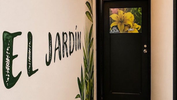 A hallway with a wall-mounted sign reading 'EL JARDIN' and a door with a framed picture of yellow flowers. - Hospedajes el Jardin (Envigado)