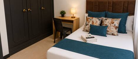 A hotel room with a bed, a desk, a chair, a lamp, and a wardrobe.