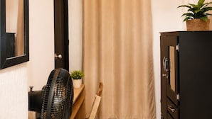 A narrow room with a wooden floor, a ceiling fan, a beige curtain, a black cabinet, and a potted plant. - Hospedajes el Jardin (Envigado)
