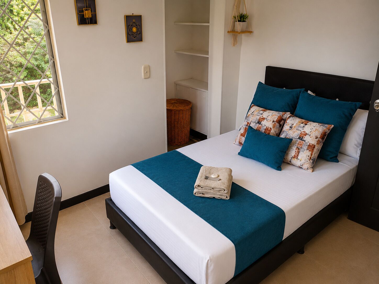 A neatly made bed with a teal bedspread, a folded towel, and multiple pillows.