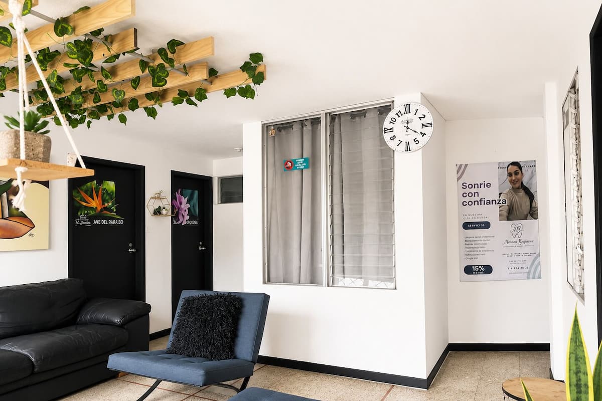 Un espace d’accueil moderne avec un canapé en cuir noir, un fauteuil bleu, une horloge et une affiche publicitaire pour une clinique dentaire.
