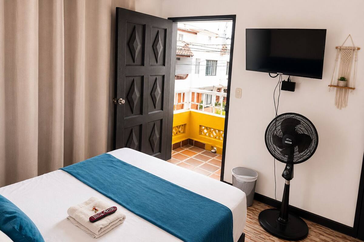 Une chambre d’hôtel avec un lit, une télévision, un ventilateur et une porte ouverte donnant sur un balcon.