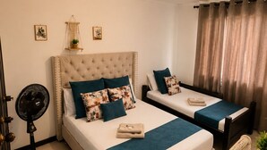 A bedroom with a large bed, a smaller bed, a bedside table, a fan, and a chair. - Hospedajes el Jardin (Envigado)