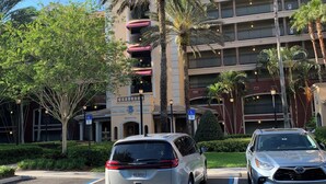 Un parking avec deux voitures, des palmiers et un immeuble à plusieurs étages doté de balcons.