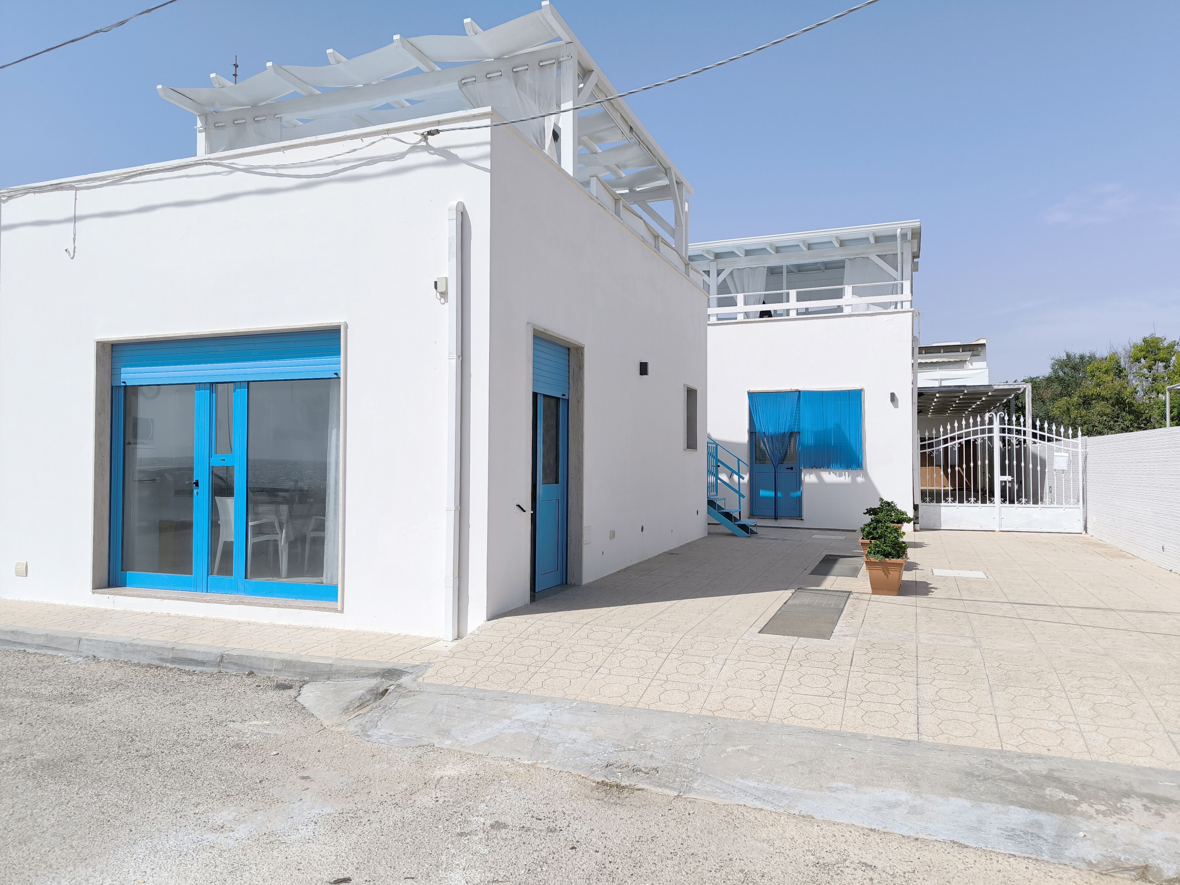 A white building with blue doors and windows, a covered outdoor area, and a gated entrance.