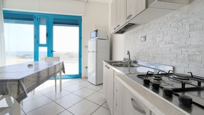 Cocina moderna con estufa a gas, microondas y lavaplatos. Cuenta con una mesa de comedor, una silla y vistas al exterior a través de una puerta con marcos azules.