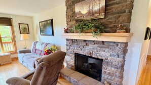 A living room with a stone fireplace, a grey armchair, and a wooden floor. - Clara's Cabin (Galax)
