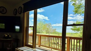 A room with a large window, a bench, and a television on the wall. - Clara's Cabin (Galax)