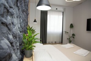 Ein modernes Hotelzimmer mit einem Bett, einer Zimmerpflanze, einem an der Wand montierten Fernseher und einem Fenster mit Vorhängen.