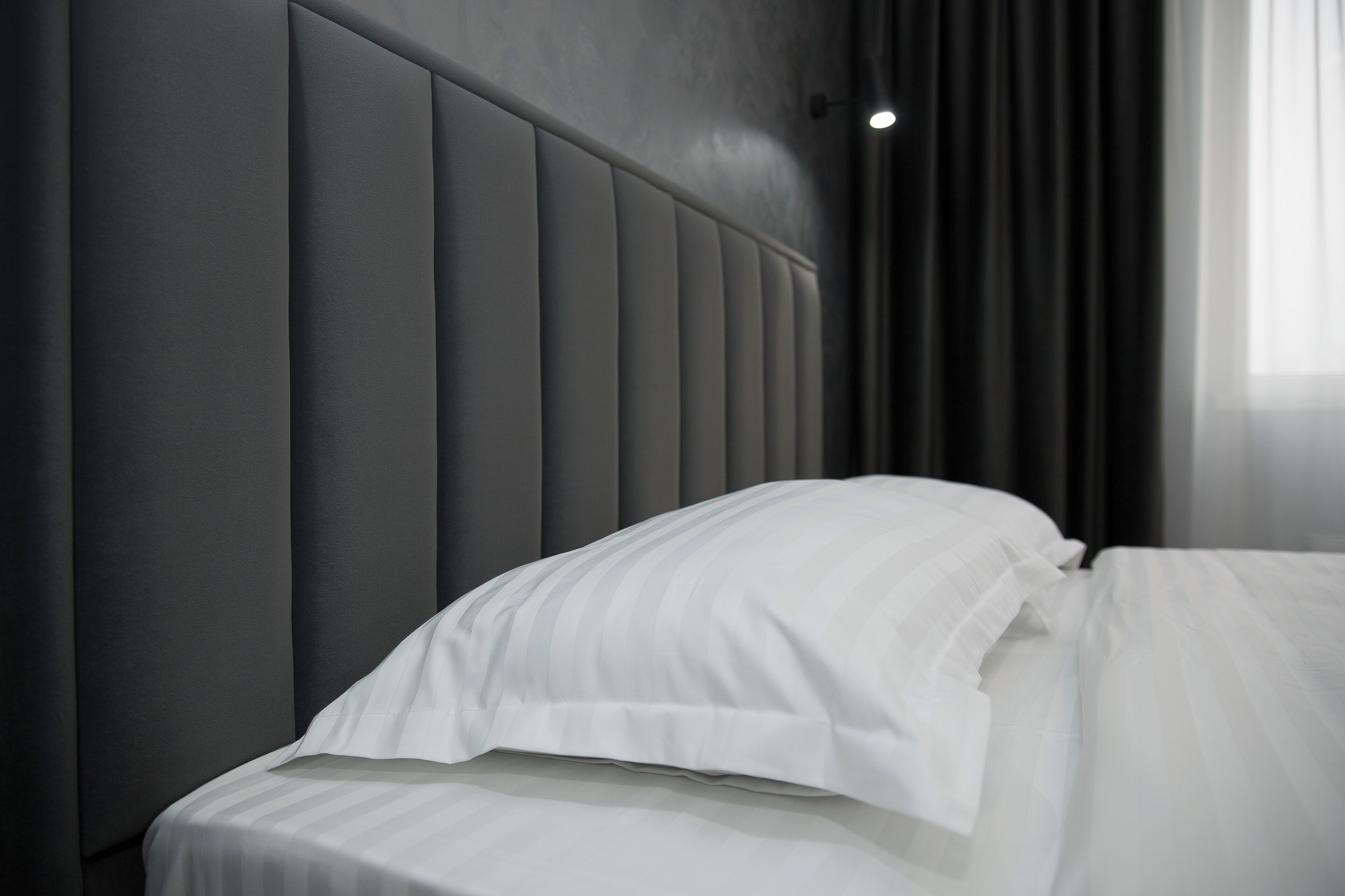 A modern hotel room with a padded headboard, a neatly made bed with white linens, and a window with dark curtains.