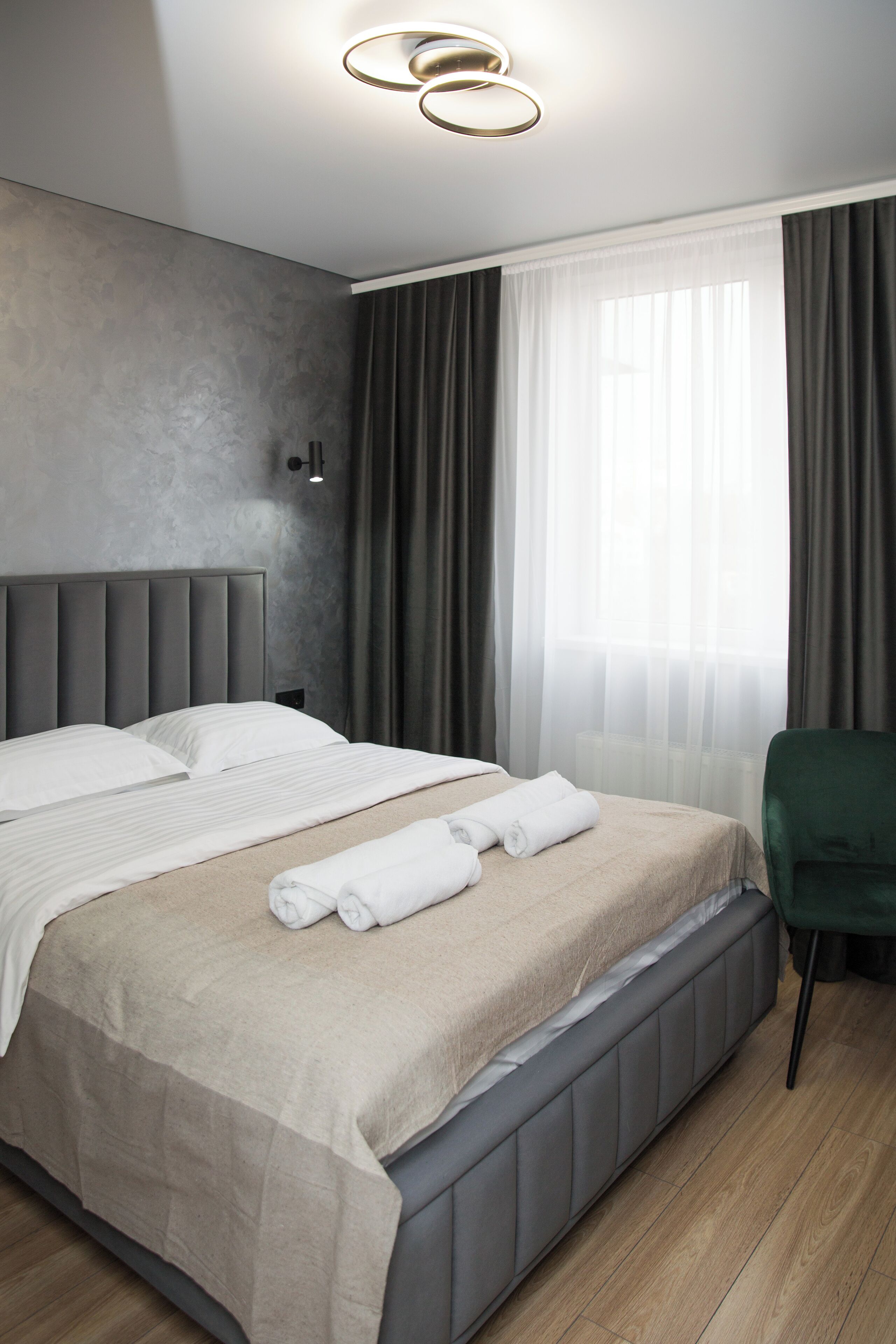 A modern hotel room with a large bed, grey headboard, and a green chair.