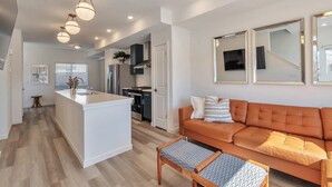 A modern living room with a sofa, a coffee table, and a kitchen area with a stove and cabinets. - Charming 3-bedroom, 4 Bath Townhome in Arvada, CO (Arvada)