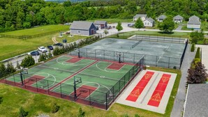 An outdoor basketball court with multiple courts, surrounded by a fence, and adjacent to a building with a red and white design. - The Snowberry - 67 Butternut (Prince Edward)