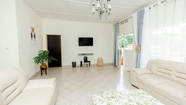 A living room with a sofa, a coffee table, a TV, and a chandelier. - Stay in Style! Elegant 4-Bedroom Home in Kigali with Fast WiFi (Kigali)