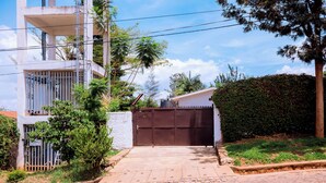 A residential building with a gated driveway, a white exterior, and a stone-paved entrance. - Stay in Style! Elegant 4-Bedroom Home in Kigali with Fast WiFi (Kigali)
