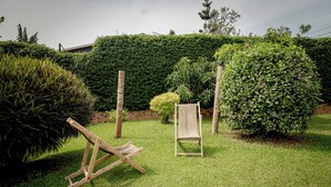 A well-maintained garden with a wooden chair and a small table, surrounded by neatly trimmed hedges and a variety of plants. - Stay in Style! Elegant 4-Bedroom Home in Kigali with Fast WiFi (Kigali)