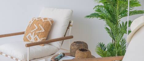 A white chair with a woven pillow, a small woven basket, and a potted plant.
