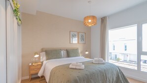 Camera da letto moderna con un letto grande, lampade ai comodini, un lampadario e vista all'esterno.