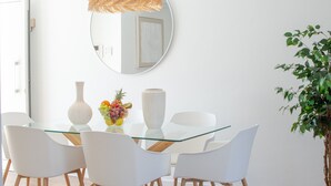 Un'area pranzo moderna con tavolo in vetro, sedie bianche, un grande specchio e una lampada a sospensione.