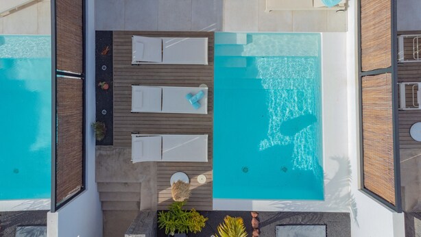 Vista aerea di una moderna area piscina esterna con due piscine separate, un solarium in legno e poltrone relax.