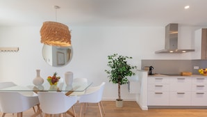 Una cocina moderna con armarios blancos, una mesa de comedor de vidrio y una lámpara colgante.