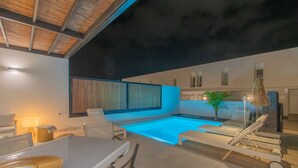 Un área interior de piscina moderna con sillones, una mesa y una pequeña zona de estar.