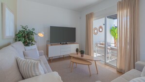 Una sala moderna con una televisión de pantalla plana, un sofá, una mesa de centro y un comedor con un puerta de vidrio que da a un espacio exterior.