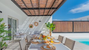 A dining area with a table set for breakfast, overlooking a pool. - Villa Serena Luca (Playa Blanca)