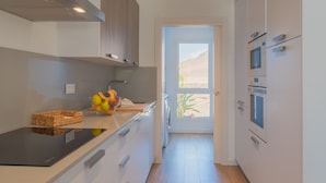 A modern kitchen with white cabinets, a black countertop, and a window leading to a desert view. - Villa Serena Luca (Playa Blanca)