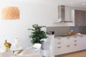 A modern kitchen with white cabinets, a glass table, and a hanging light fixture.