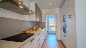 Une cuisine moderne avec des meubles blancs, une plaque de cuisson à induction noire et un pare-feu en bois.