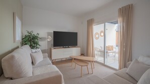 Un salon moderne avec un canapé, un téléviseur posé sur un meuble blanc, une table basse et une porte-fenêtre coulissante donnant sur un espace extérieur.