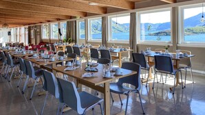 A spacious dining area with multiple tables and chairs, large windows offering scenic views of a lake and mountains, and wooden ceiling beams. - 2 bedroom lovely home in ørsta (Ørsta)