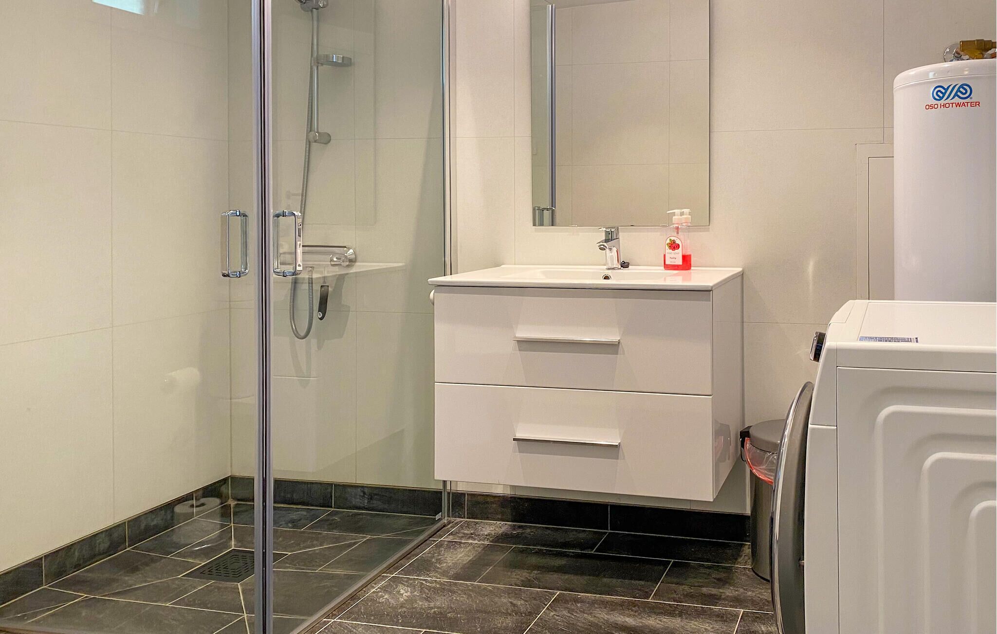 A modern bathroom with a glass shower enclosure, a white sink with a mirror above it, and a white washing machine.