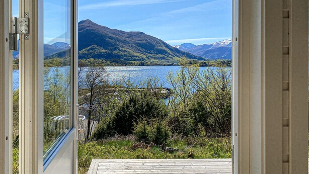 A view from a room with a glass door, overlooking a lake, mountains, and a wooden deck.
