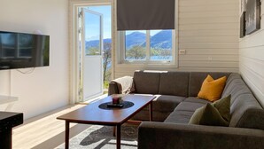 A living room with a sofa, a coffee table, a TV, and a window with a view of mountains.