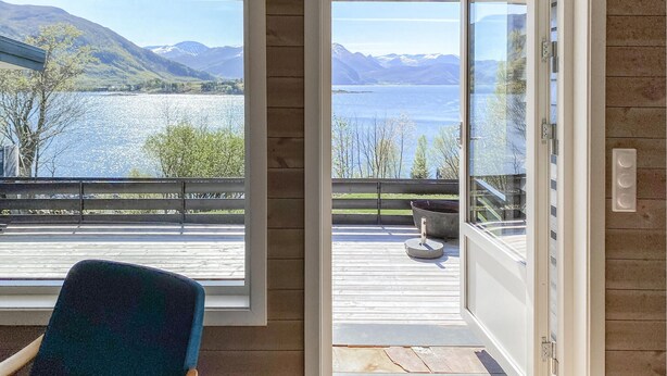 Habitación con vistas a un lago y montañas. En el balcón, hay una silla y una mesa con un bol.