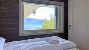 Un dormitorio con un amplio ventanal con vistas a un lago y montañas.