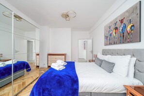A modern hotel room with a large bed, a mirror, a painting, and a wooden floor.