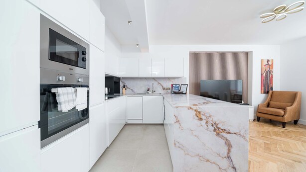 Una cocina moderna con armarios blancos, una isla de mármol y un horno empotrado.