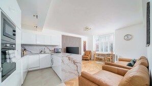 Una cocina moderna con armarios blancos, una isla de mármol y un televisor de pantalla plana.
