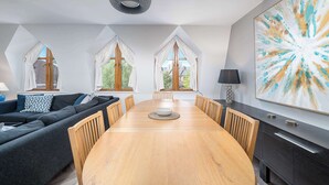A modern dining room with a wooden table, dark sofas, and large windows with white curtains. - Beautiful 2 bed flat near Battersea park (London)