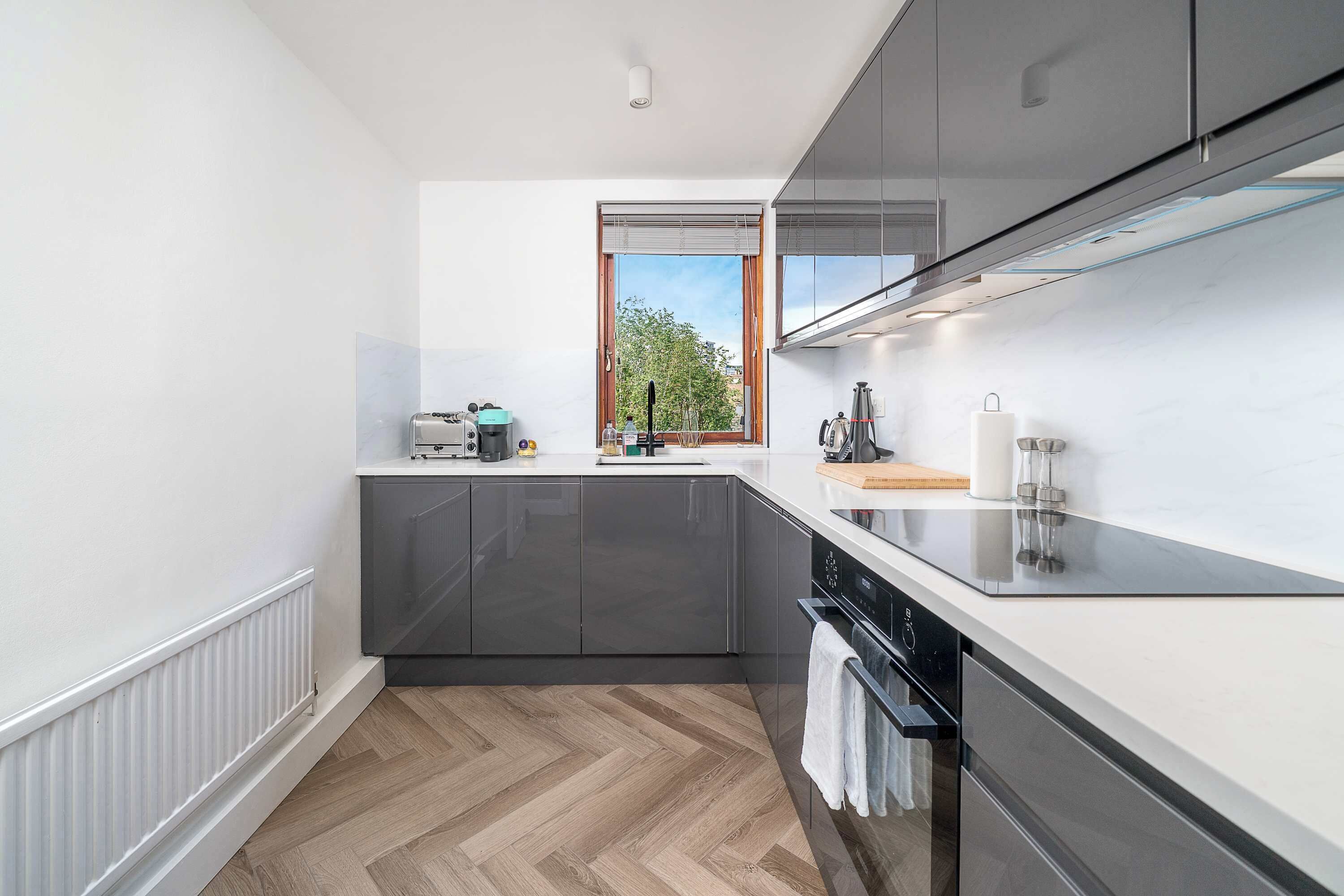 Une cuisine moderne avec des meubles de couleur sombre, un plan de travail noir et une fenêtre donnant sur des arbres.