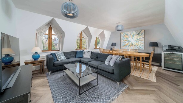 A modern living room with a sectional sofa, a glass coffee table, and a dining area with a wooden table and chairs. - Beautiful 2 bed flat near Battersea park (London)
