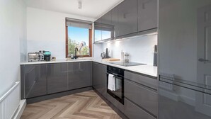 A modern kitchen with stainless steel appliances, a herringbone wood floor, and a window with a city view. - Beautiful 2 bed flat near Battersea park (London)