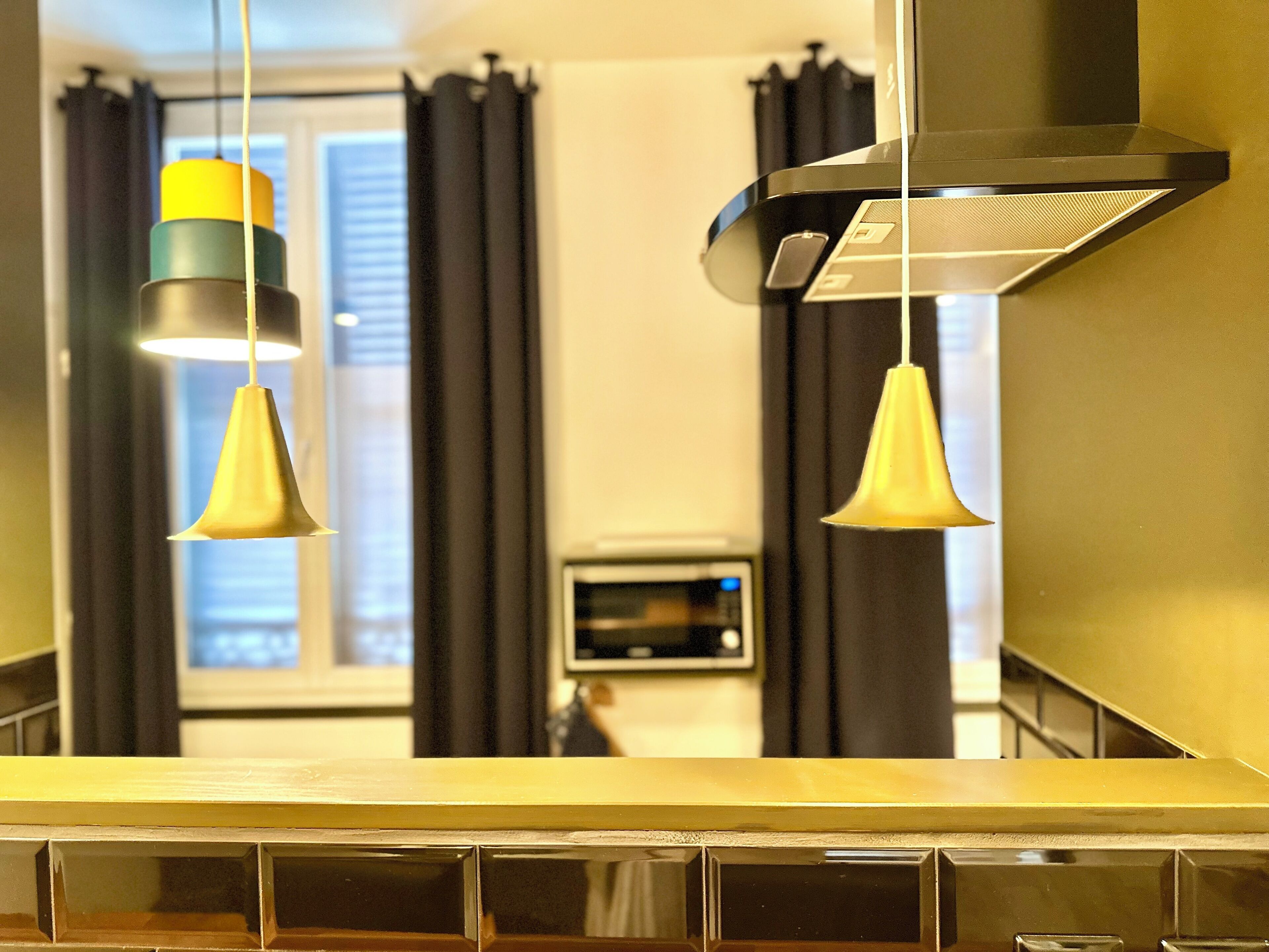 A kitchen with a microwave, hanging pendant lights, and a stove hood.