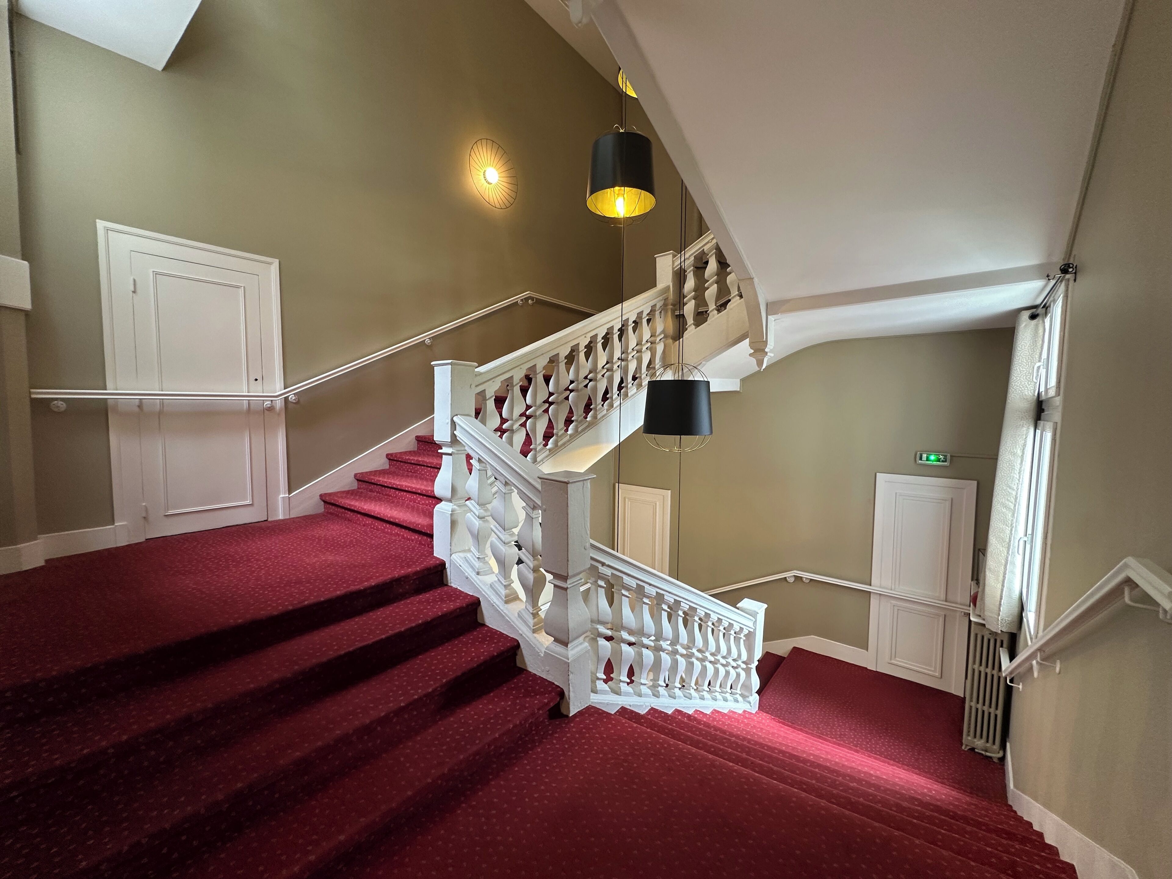 Eine imposante Treppe mit roten Teppichstufen, weißen Wangen und einer schwarzen Pendelleuchte.