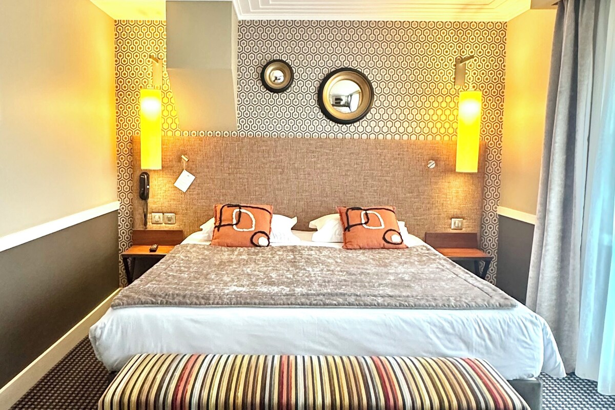 Une chambre d’hôtel avec un grand lit, deux tables de chevet, une tête de lit agrémentée d’un miroir et des murs à motifs.