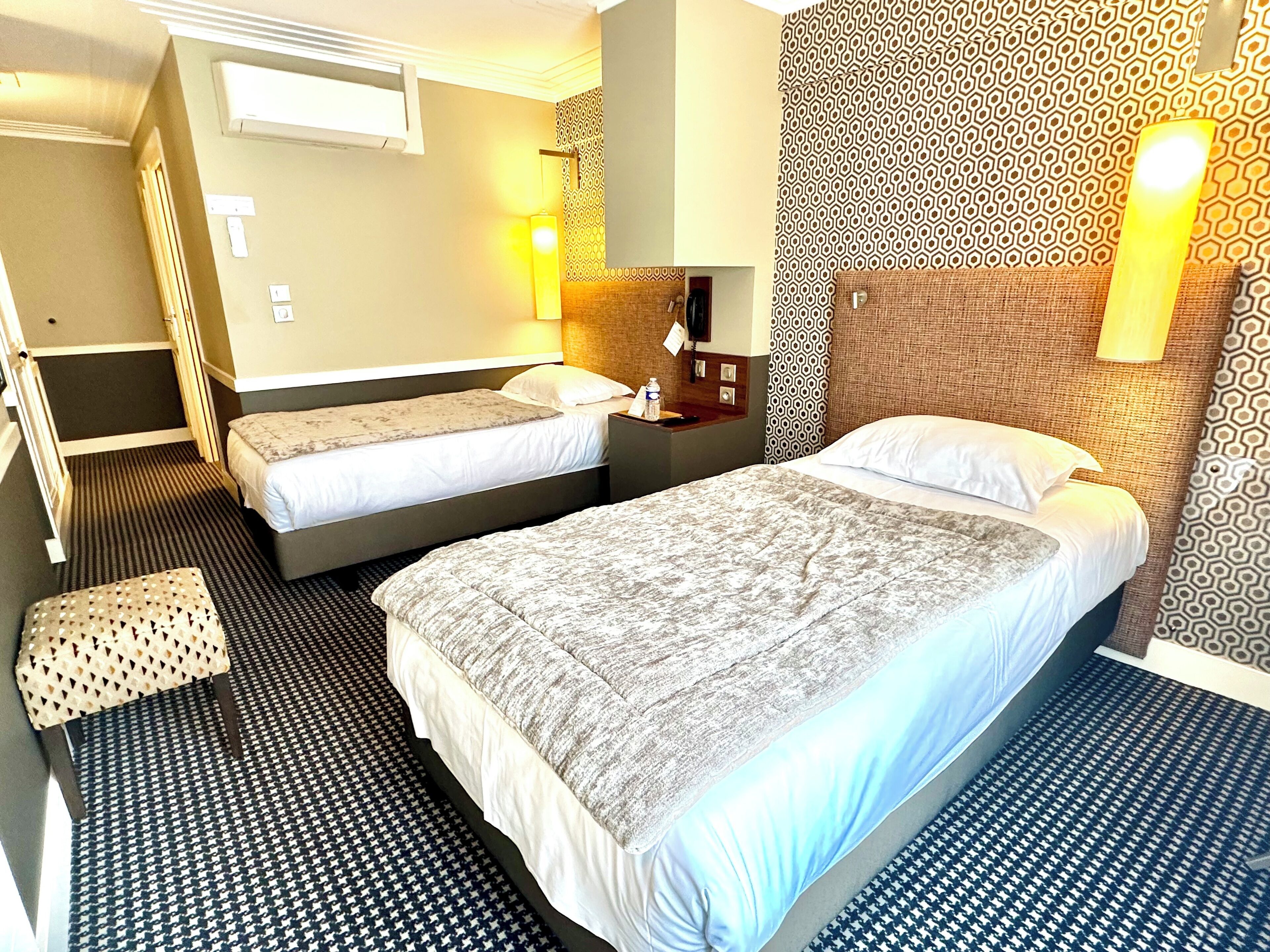 Une chambre d’hôtel avec deux lits, un petit coin salon, un bureau et un mur décoré d’un motif.