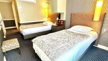 Une chambre d’hôtel avec deux lits, un petit coin salon, un bureau et un mur décoré d’un motif.